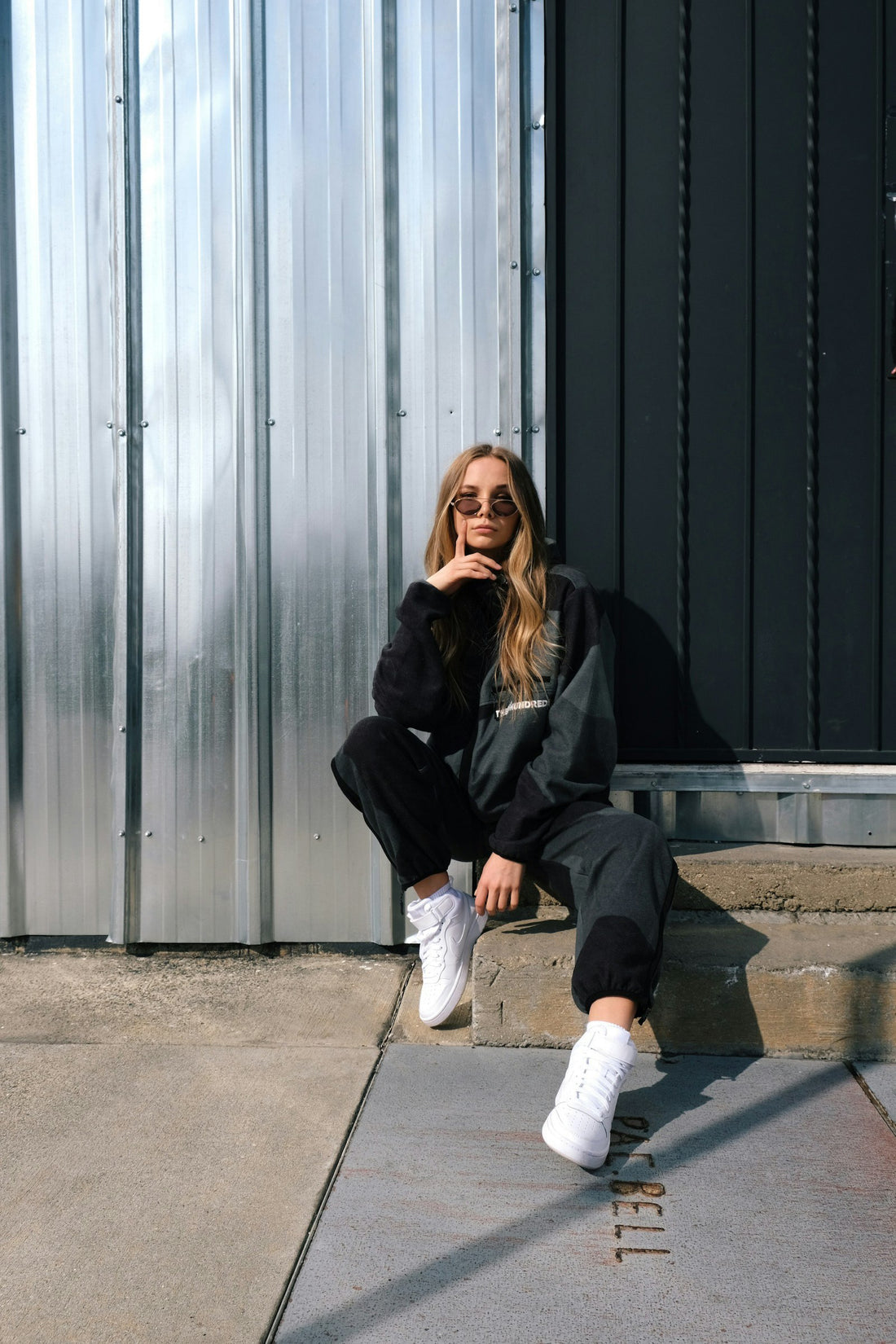 Woman in a black jacket and white pants sitting on concrete