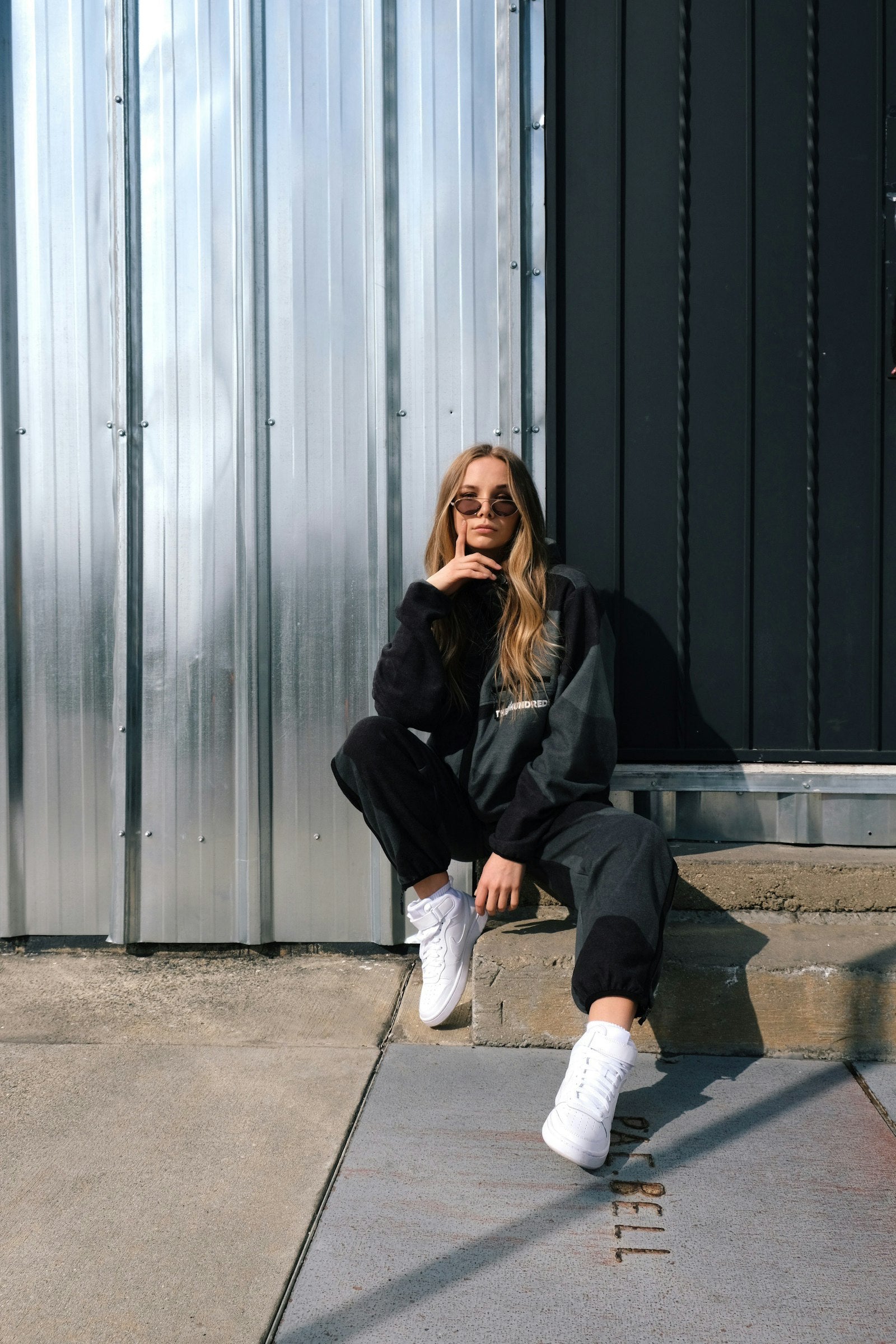 Woman in a black jacket and white pants sitting on concrete