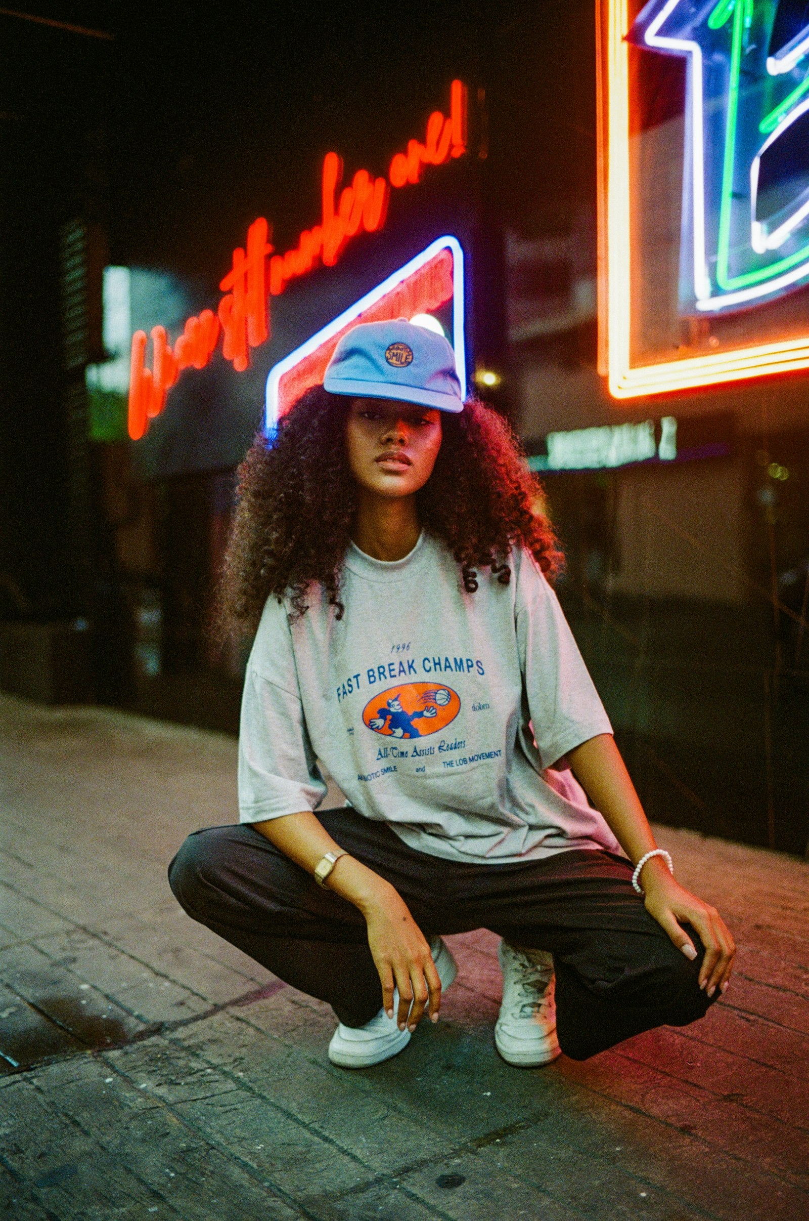 Woman sitting on the ground in front of a glowing neon sign